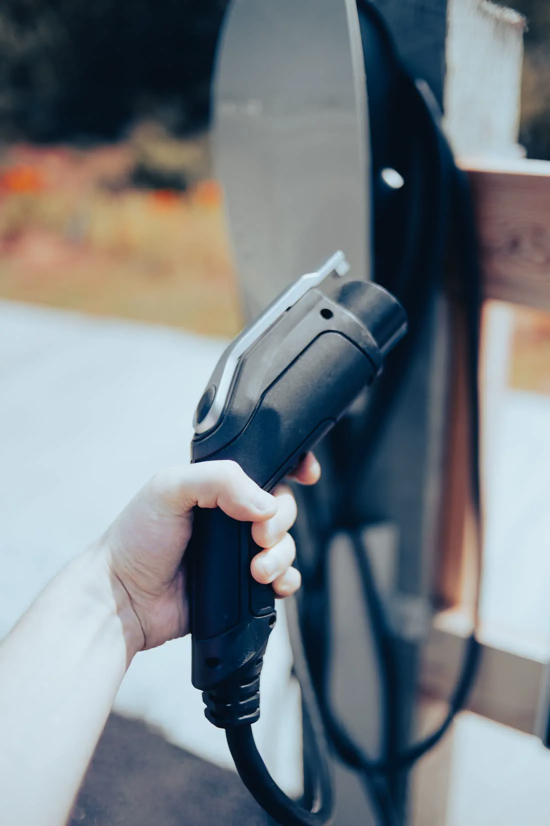 Hand holding a Type 2 EV charging plug at a home EV charger in Auckland